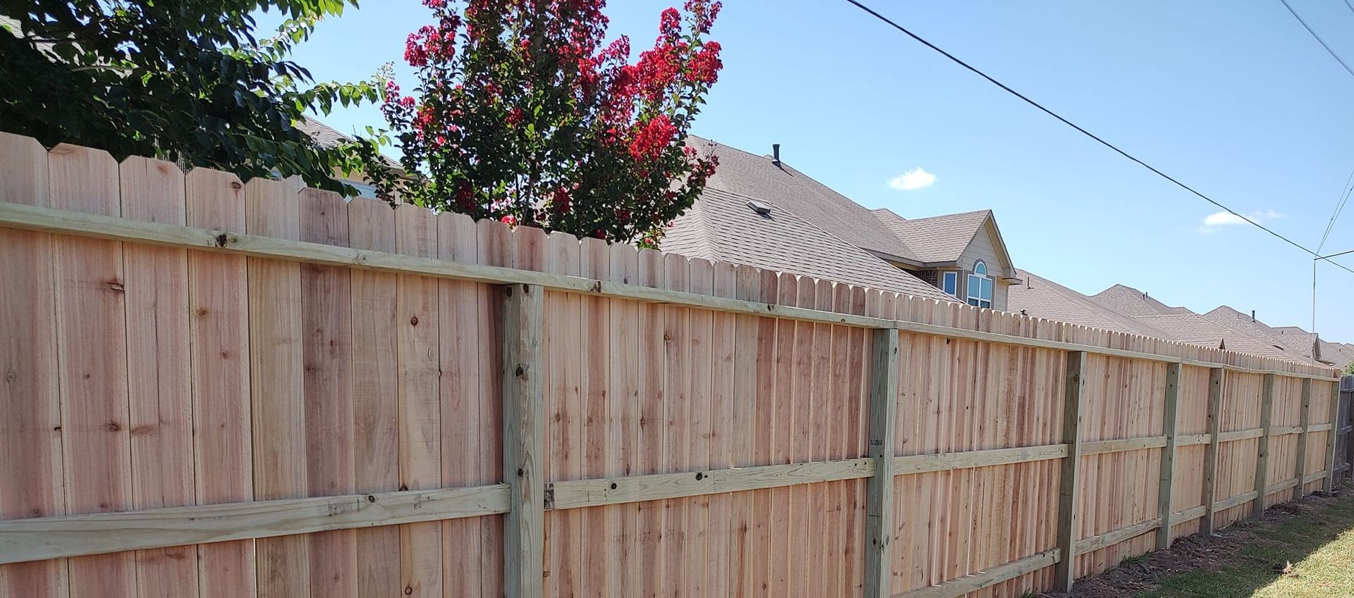A wooden fence with a house in the background and a tree in the foreground.