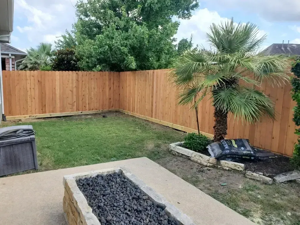 A wooden fence surrounds a backyard with a fire pit.