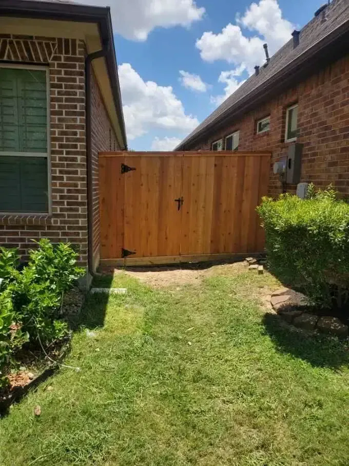A wooden fence is in the backyard of a brick house.