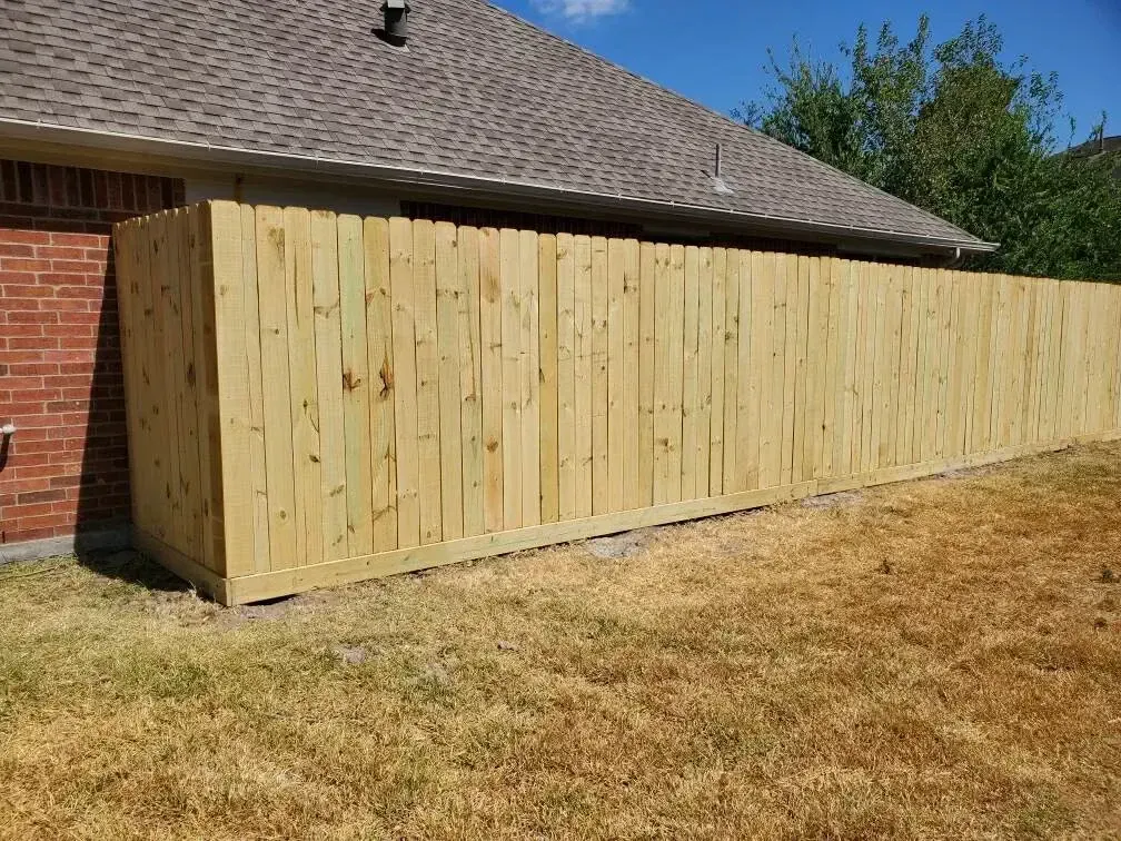 A wooden fence is sitting in front of a brick house.