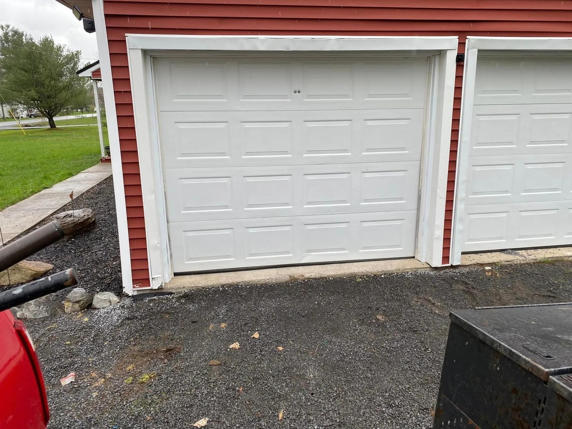 White garage door on a red building, surrounded by black gravel and a small lawn.