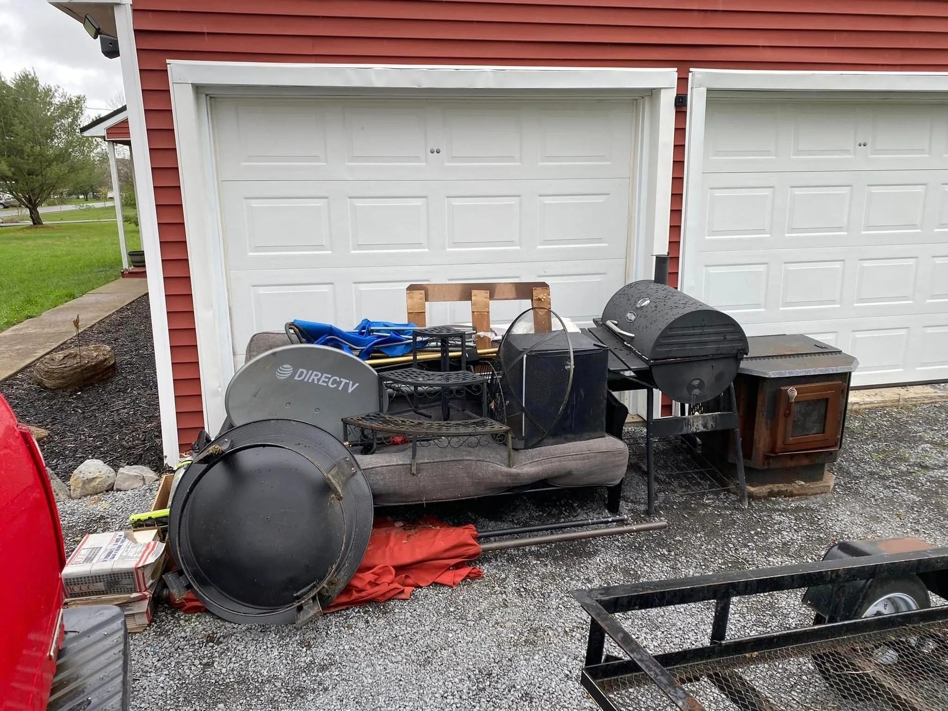 A pile of discarded items, including a satellite dish and grills, sits in front of a garage.