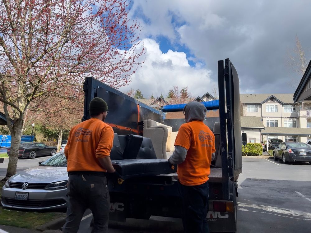 Two workers loading furniture into a truck on a sunny day near an apartment building.