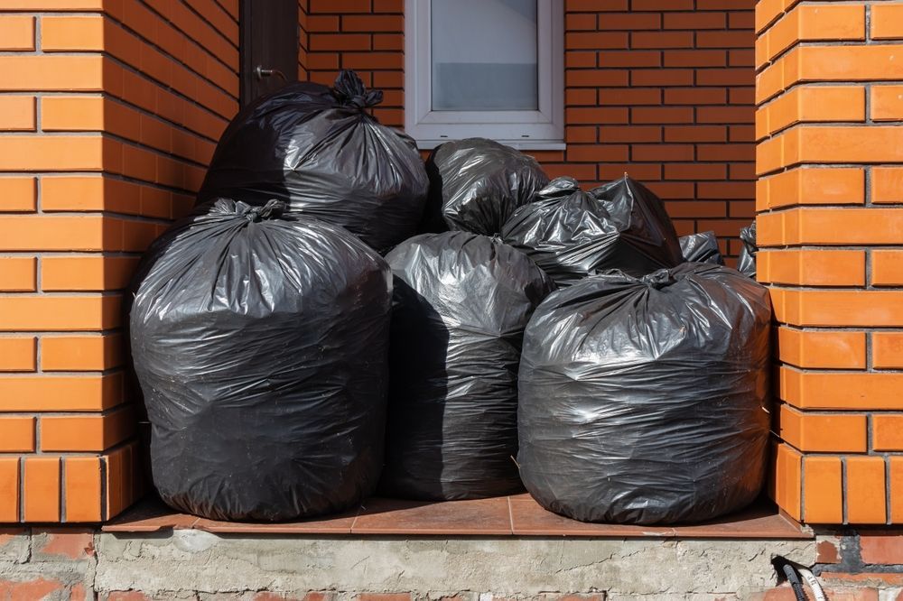 Black trash bags piled on a concrete step in front of a brick building.