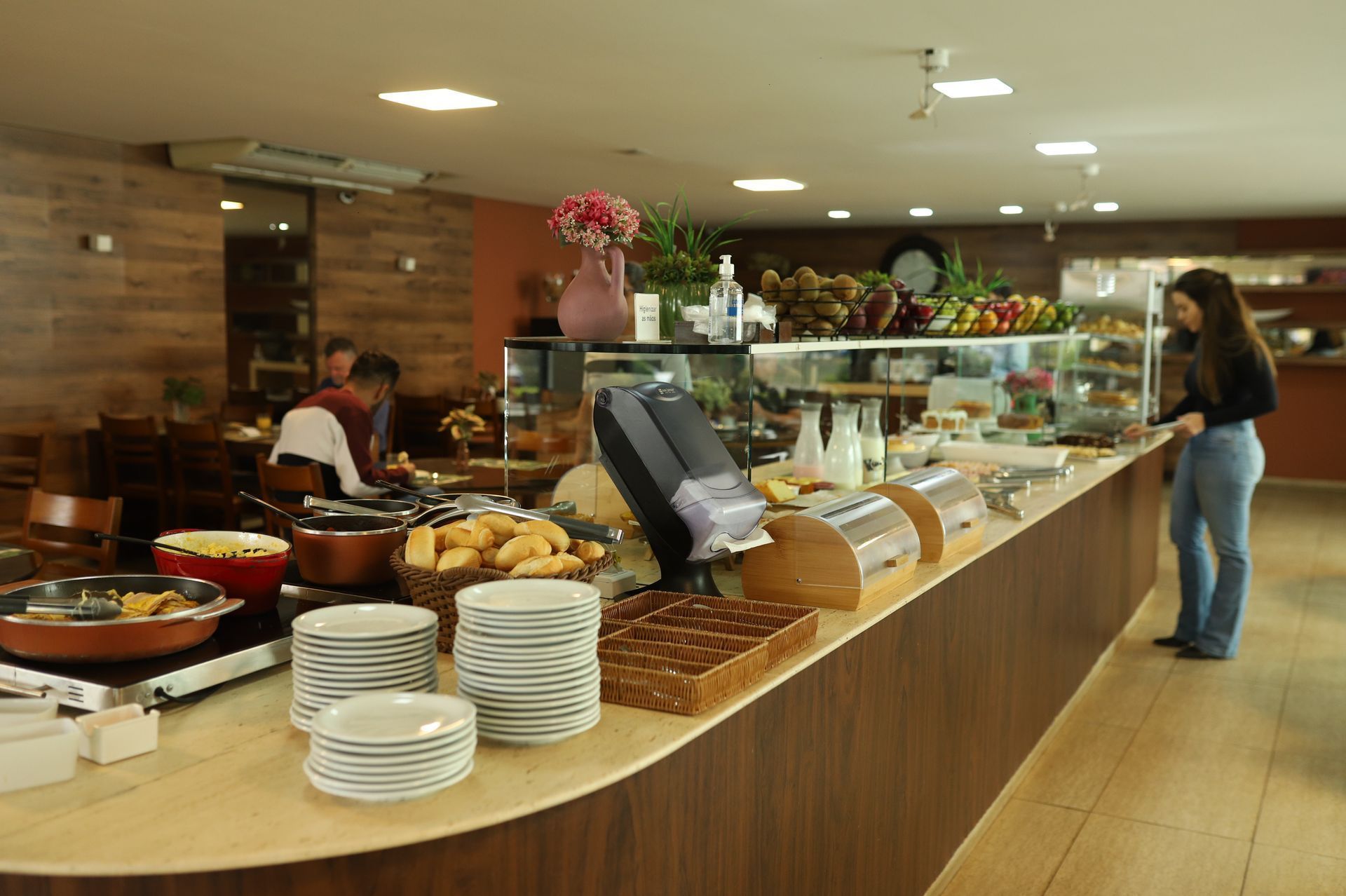 Balcão de buffet com doces e pratos empilhados em um café, com uma pessoa em pé por perto.
