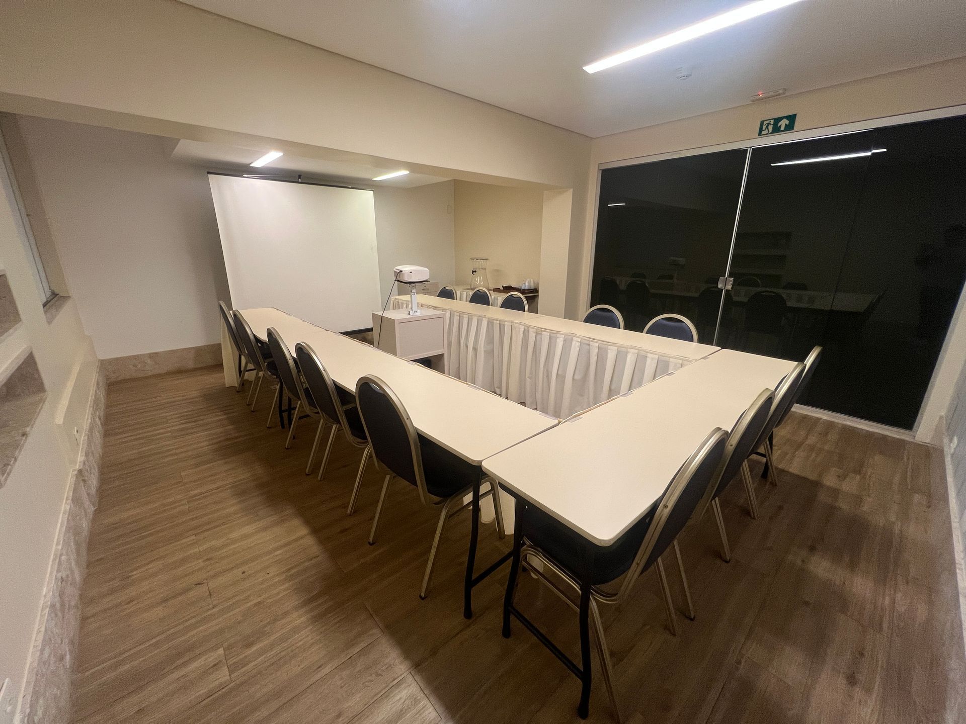 Sala de conferências com mesa em formato de U, cadeiras pretas e uma grande janela ao fundo.