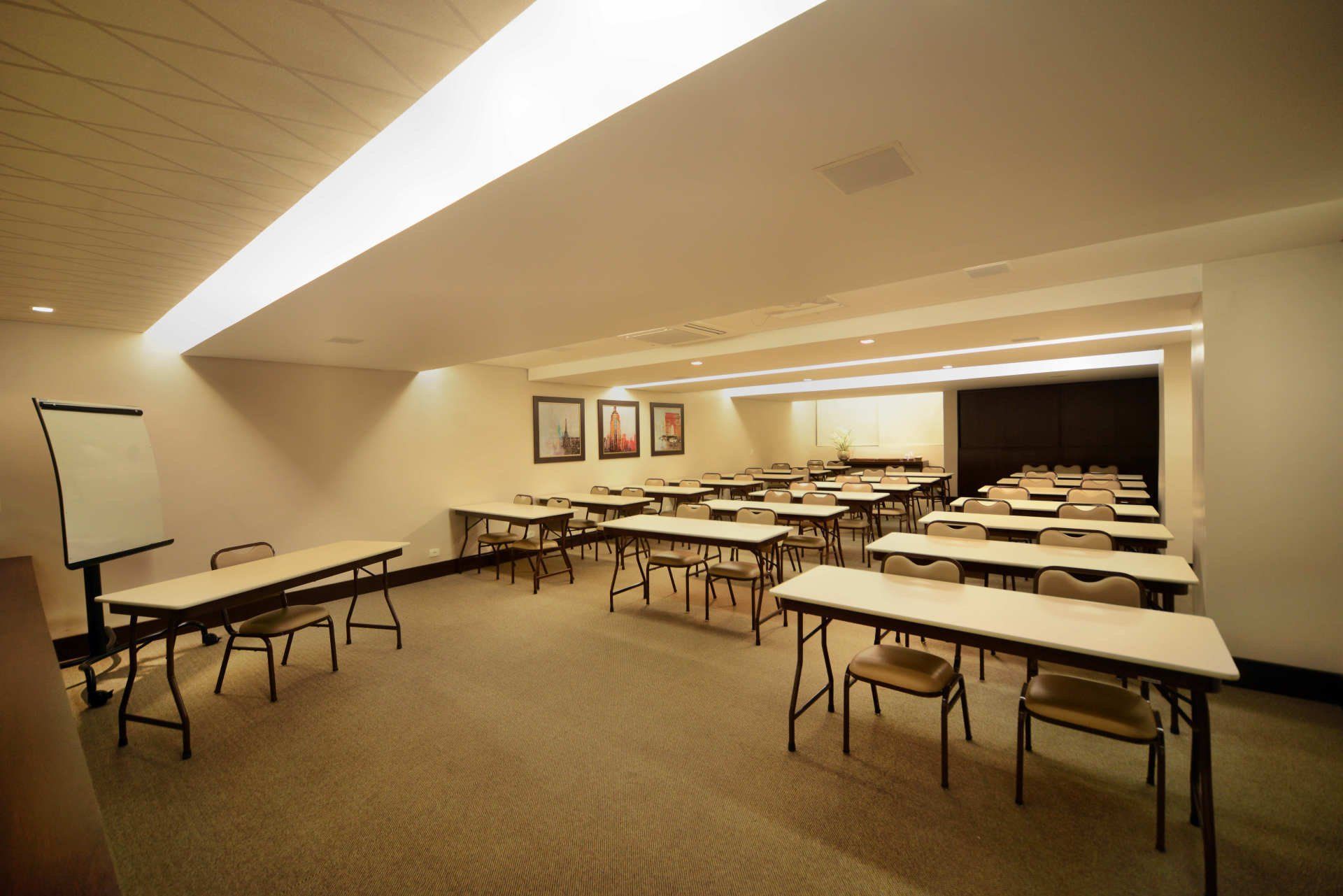 Sala de aula vazia com fileiras de mesas e cadeiras, quadro branco e tela de projeção em uma sala de conferências.