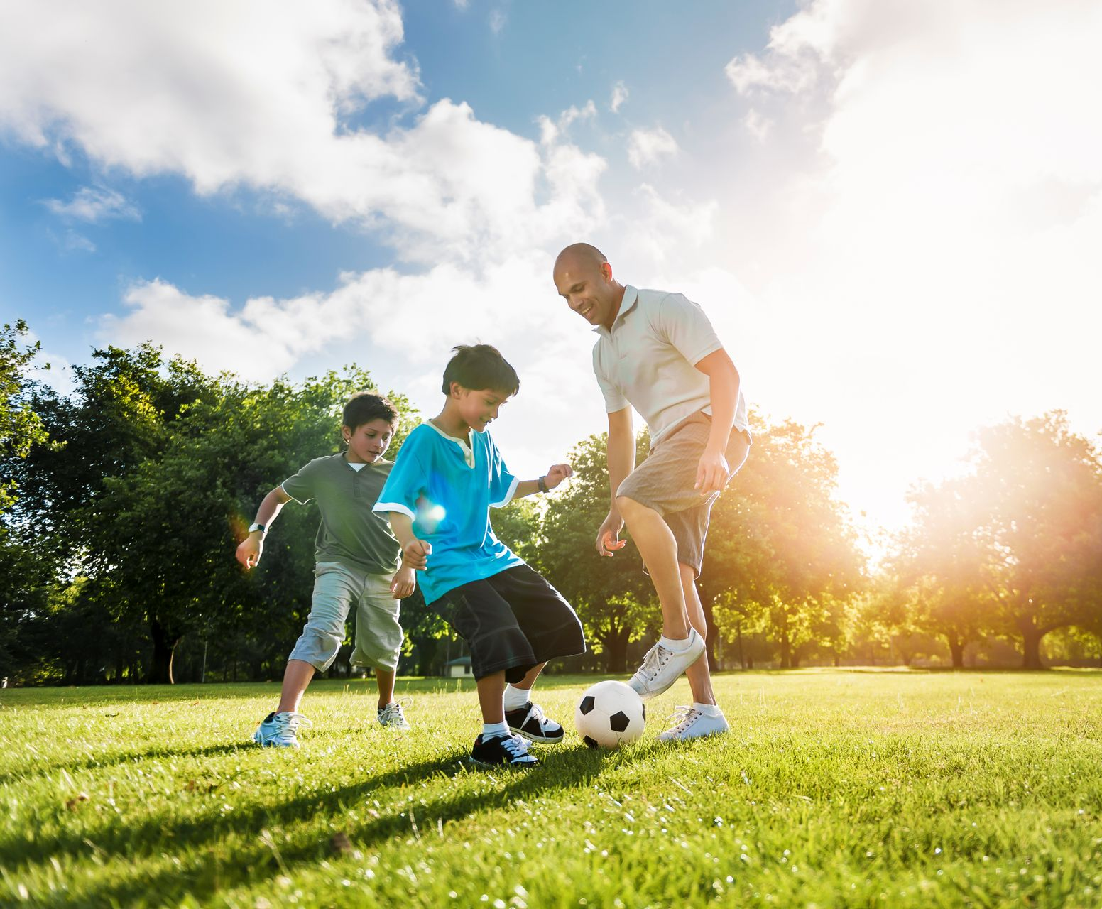 Man and two children playing soccer on a sunny, grassy field.