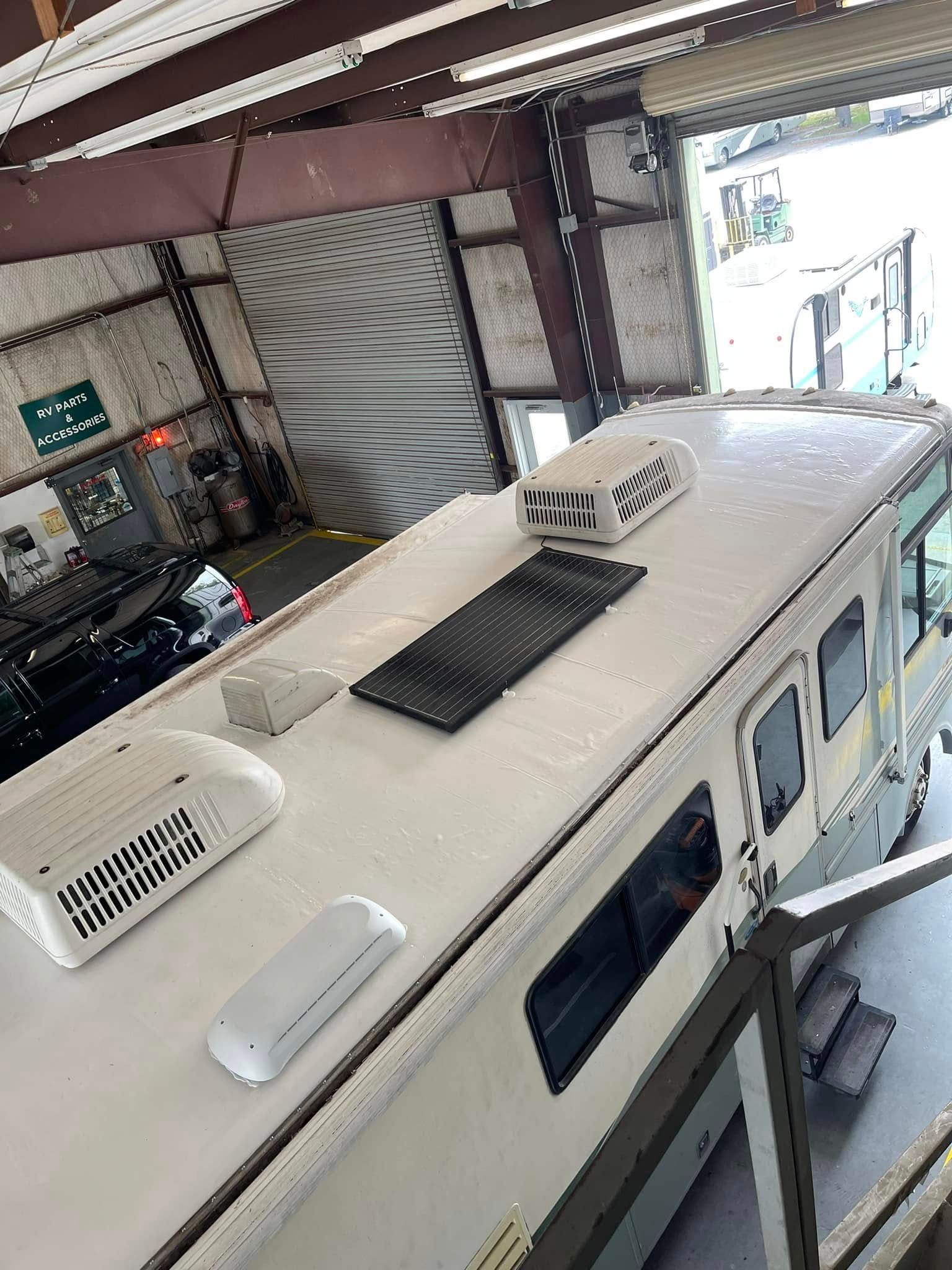 RV service bay with a large motorhome, tools on carts, and a lift in a bright workshop