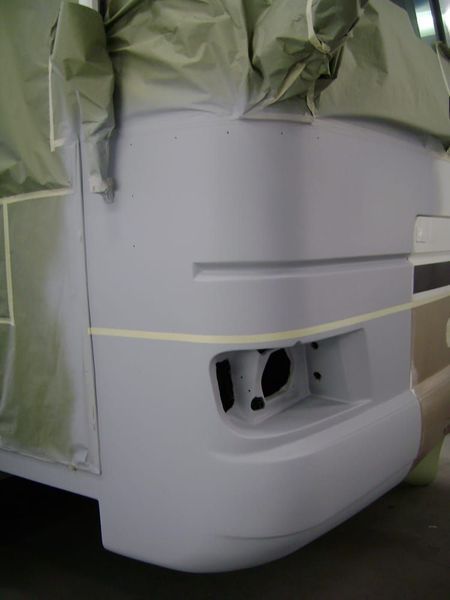 White vehicle rear corner masked with green plastic, showing an exposed rectangular light opening and yellow tape.