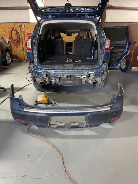 Blue SUV with rear bumper removed in a garage, showing the open hatch and detached bumper on the floor