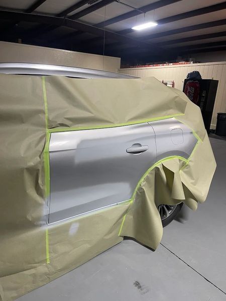 Masked silver car door in a garage, partially covered with beige masking paper and tape for painting.
