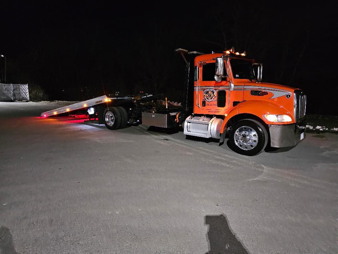 An orange tow truck is parked on the side of the road at night.