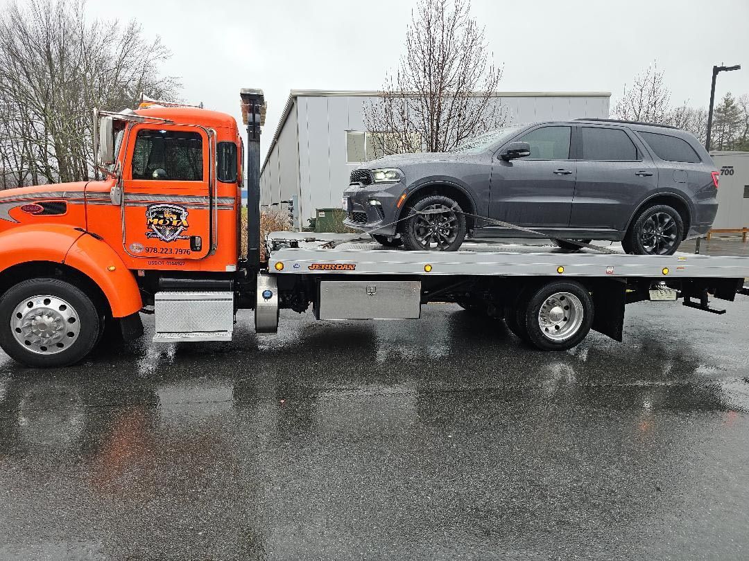 An orange tow truck is towing a gray suv.