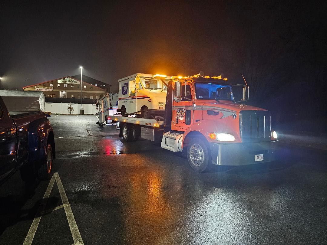 A tow truck is towing a car in a parking lot at night.