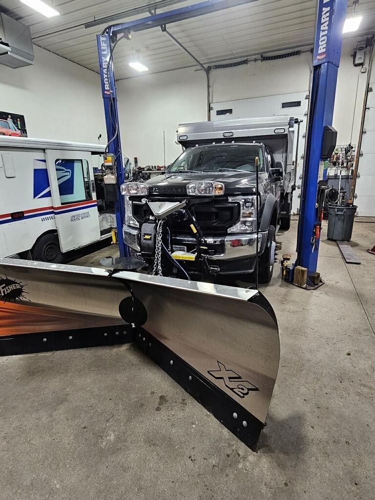 A truck is sitting on a lift in a garage with a snow plow attached to it.
