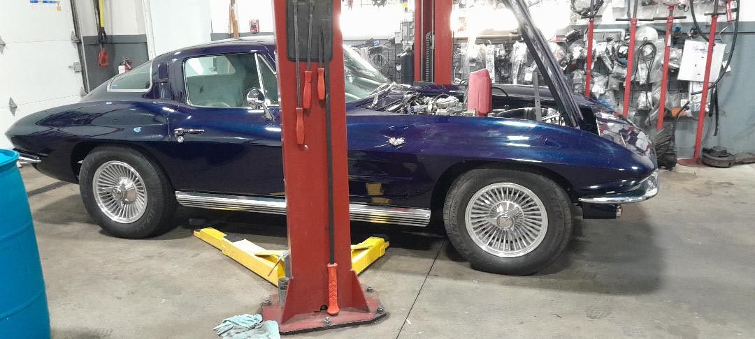 A blue corvette is sitting on a lift in a garage.