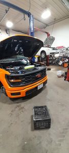 An orange truck is parked in a garage with its hood open.