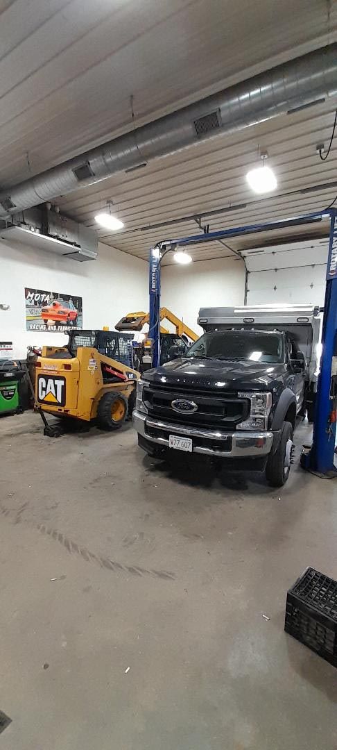A truck is parked in a garage next to a bulldozer.