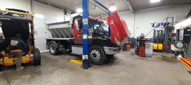 A dump truck is parked in a garage with its hood up.