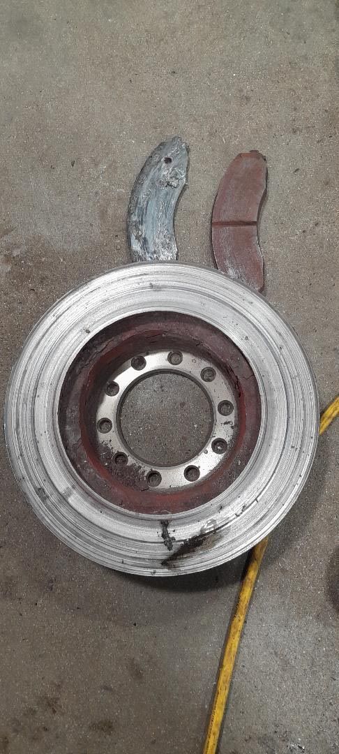 A close up of a brake disc and brake pads on a concrete floor.