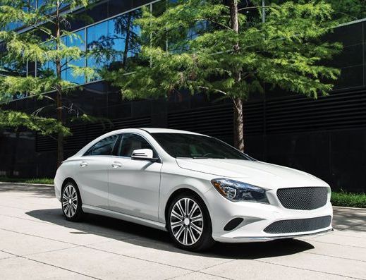 White luxury sedan parked on a paved street beside modern office buildings and trees