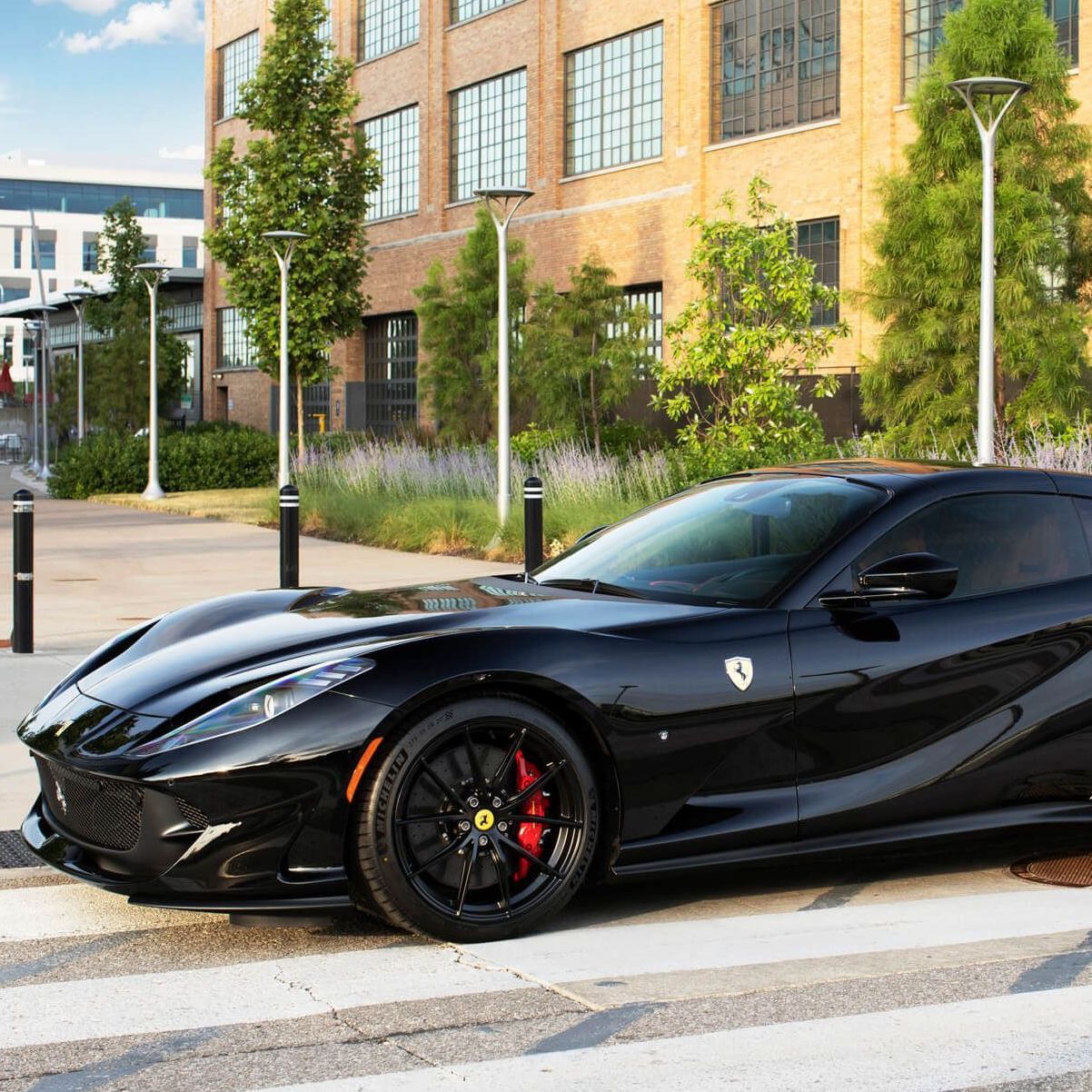 Black Ferrari sports car parked on a city street beside a brick building