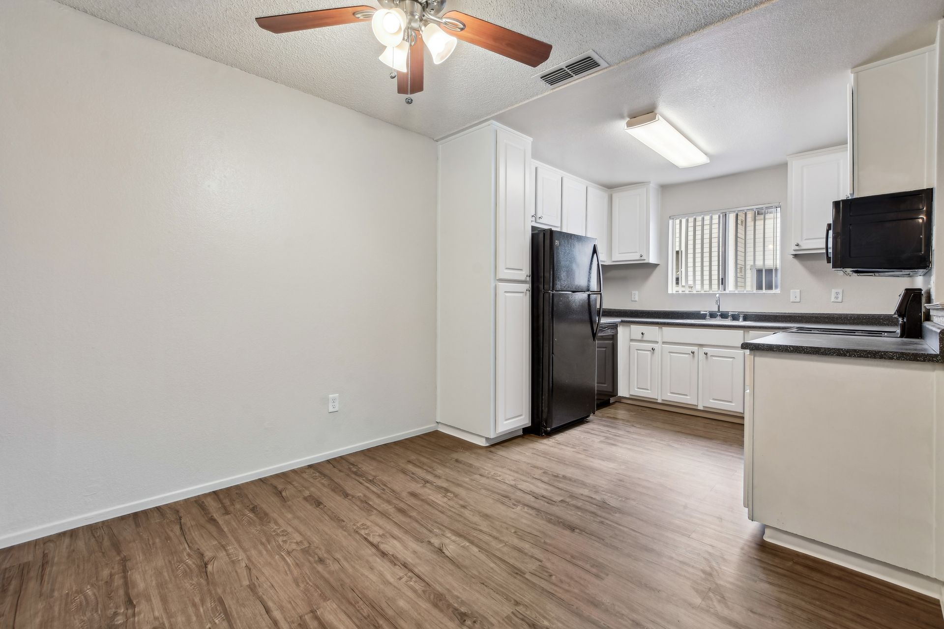 Kitchen with white cabinets, dark refrigerator, and wood-look flooring.