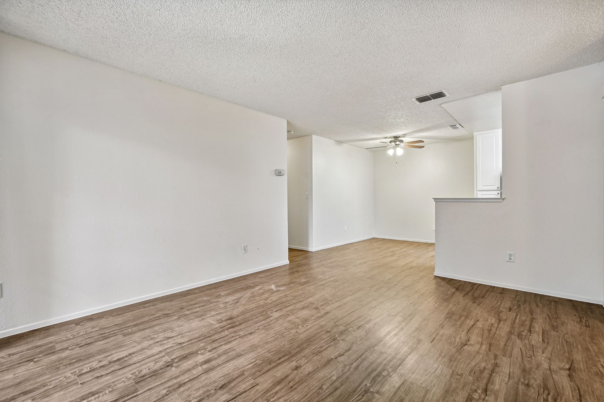 Empty living room with wood-look flooring, white walls, and a ceiling fan.