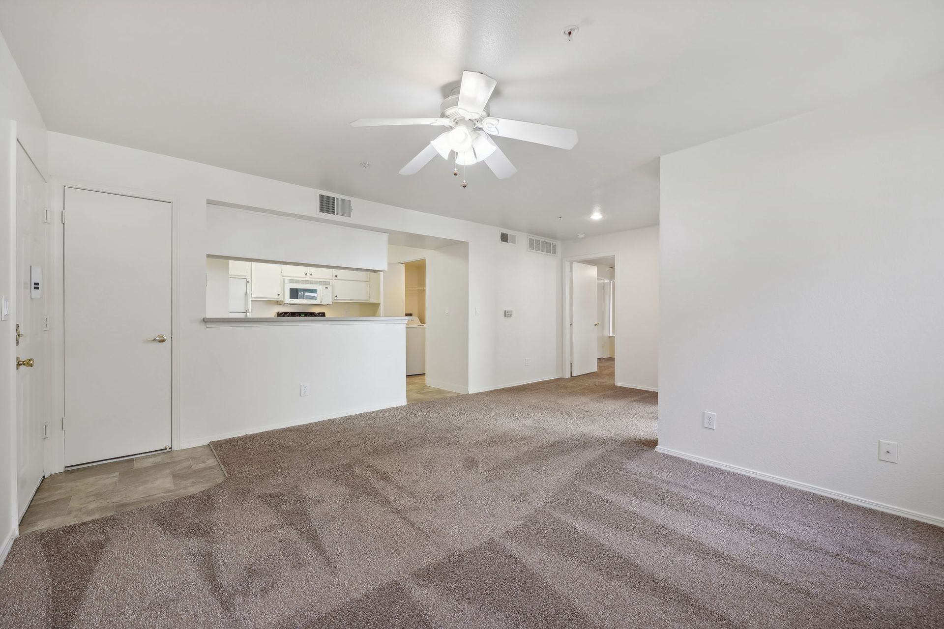 Empty living room with brown patterned carpet, white walls, and a ceiling fan.