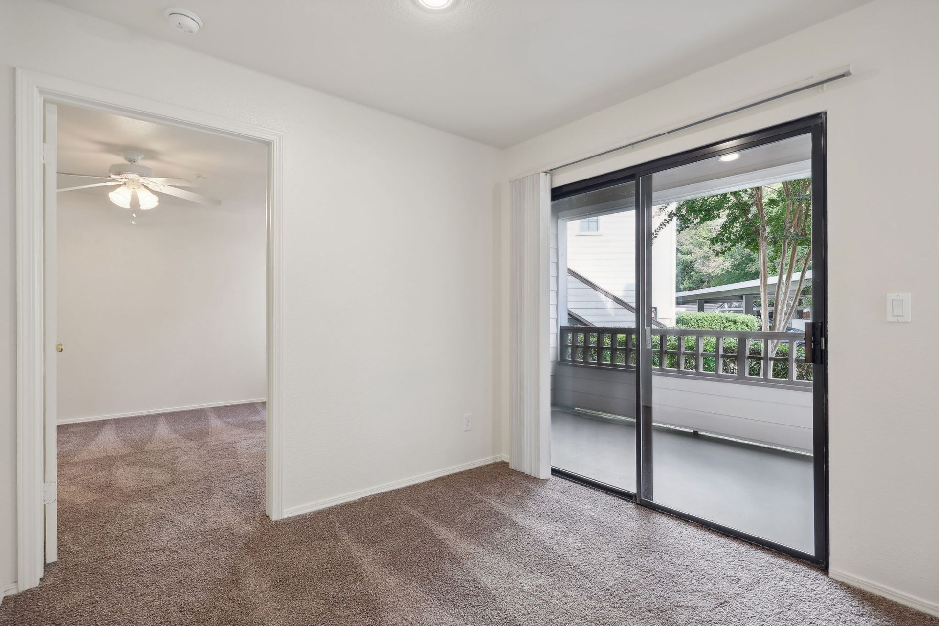Empty room with brown carpet, door to another room, sliding glass door to balcony.