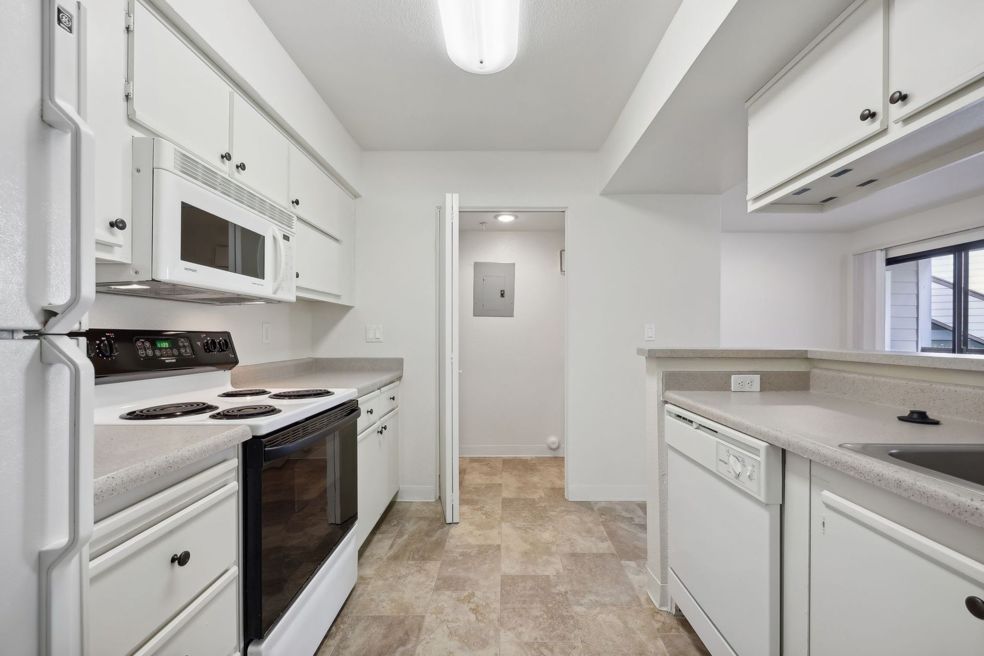 White kitchen with appliances, cabinets, and a doorway to another room.