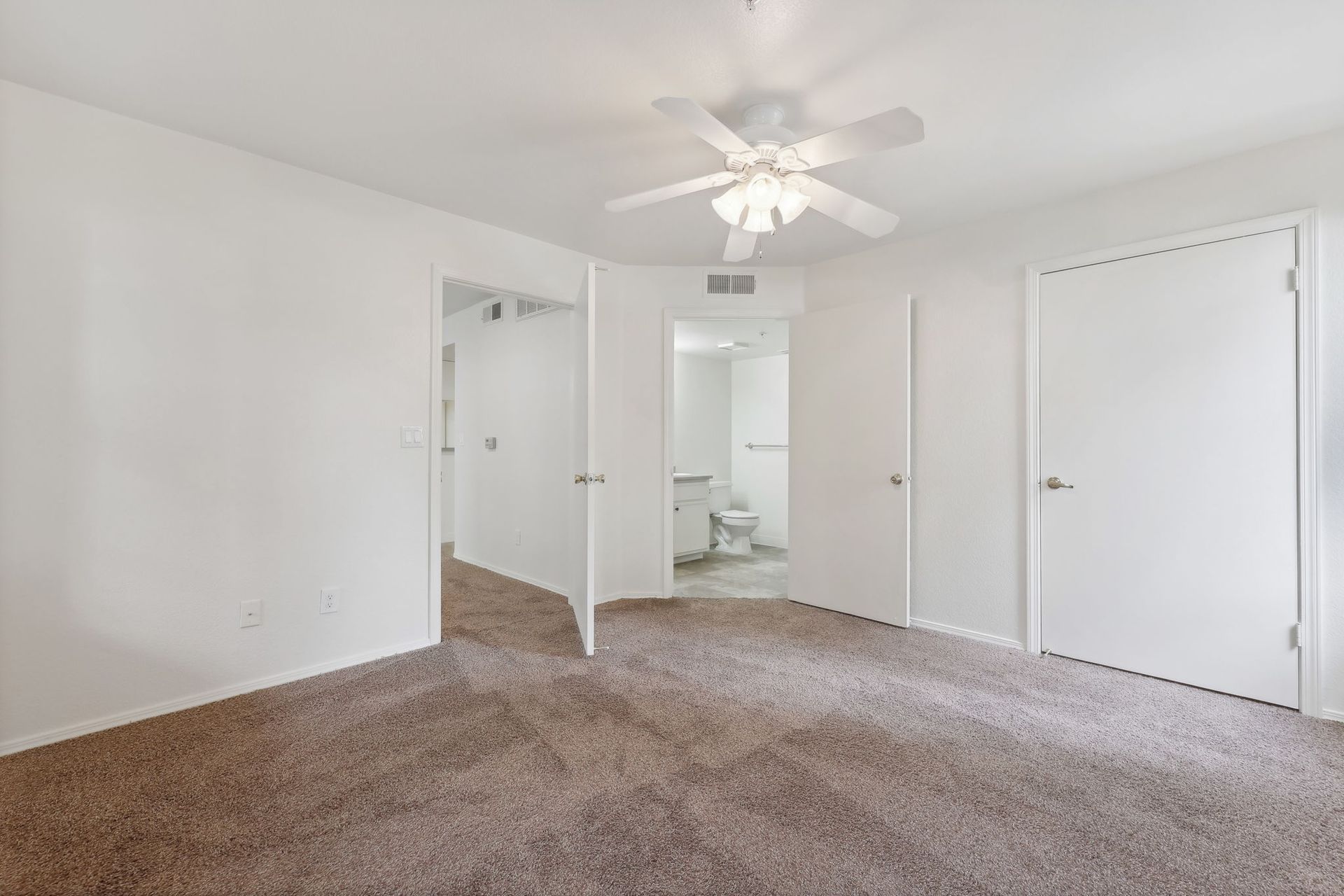 Bedroom with brown carpet, white walls, and three open doorways: closet, bathroom, and entrance.