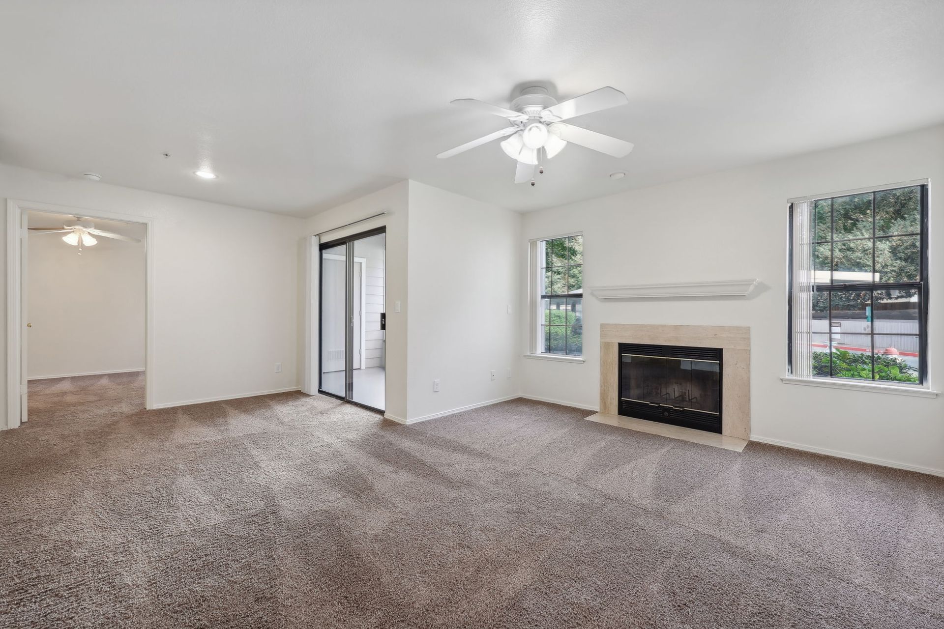 Spacious living room with carpet, a fireplace, windows, and sliding doors leading to another room.