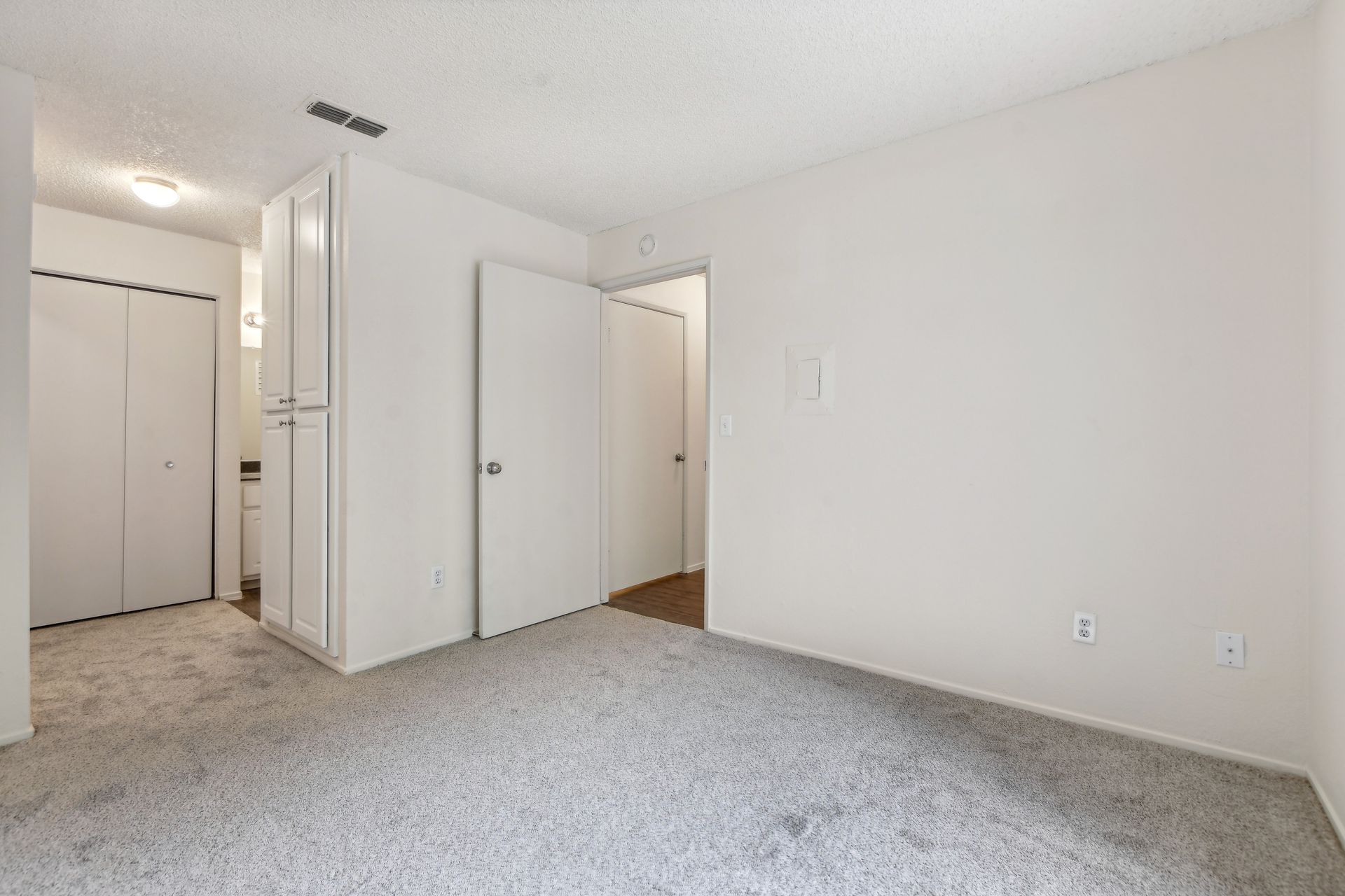 Empty bedroom with white walls, carpet, and closed doors.