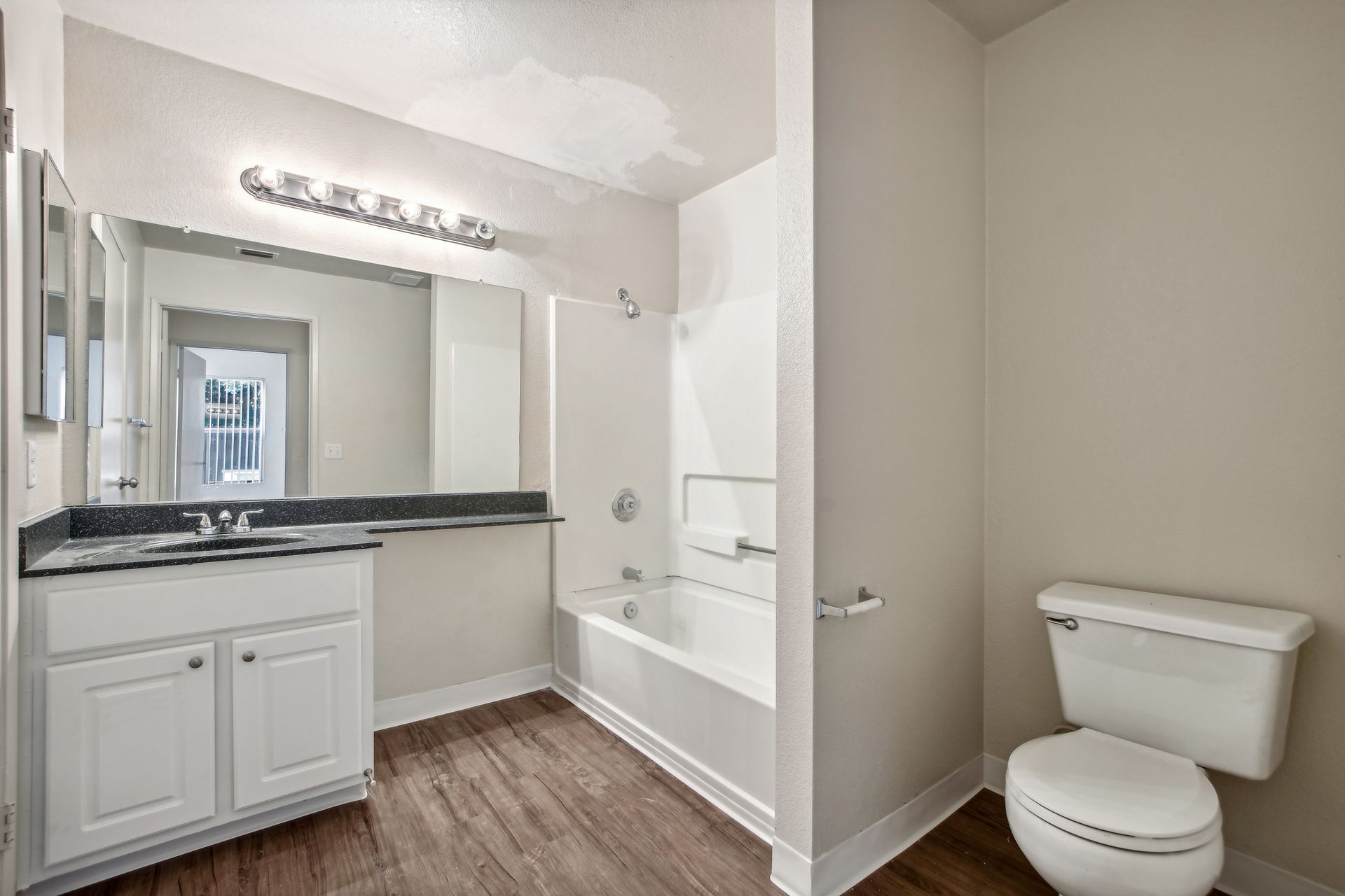Bathroom with white vanity, toilet, and bathtub. Dark wood-look flooring and light walls.