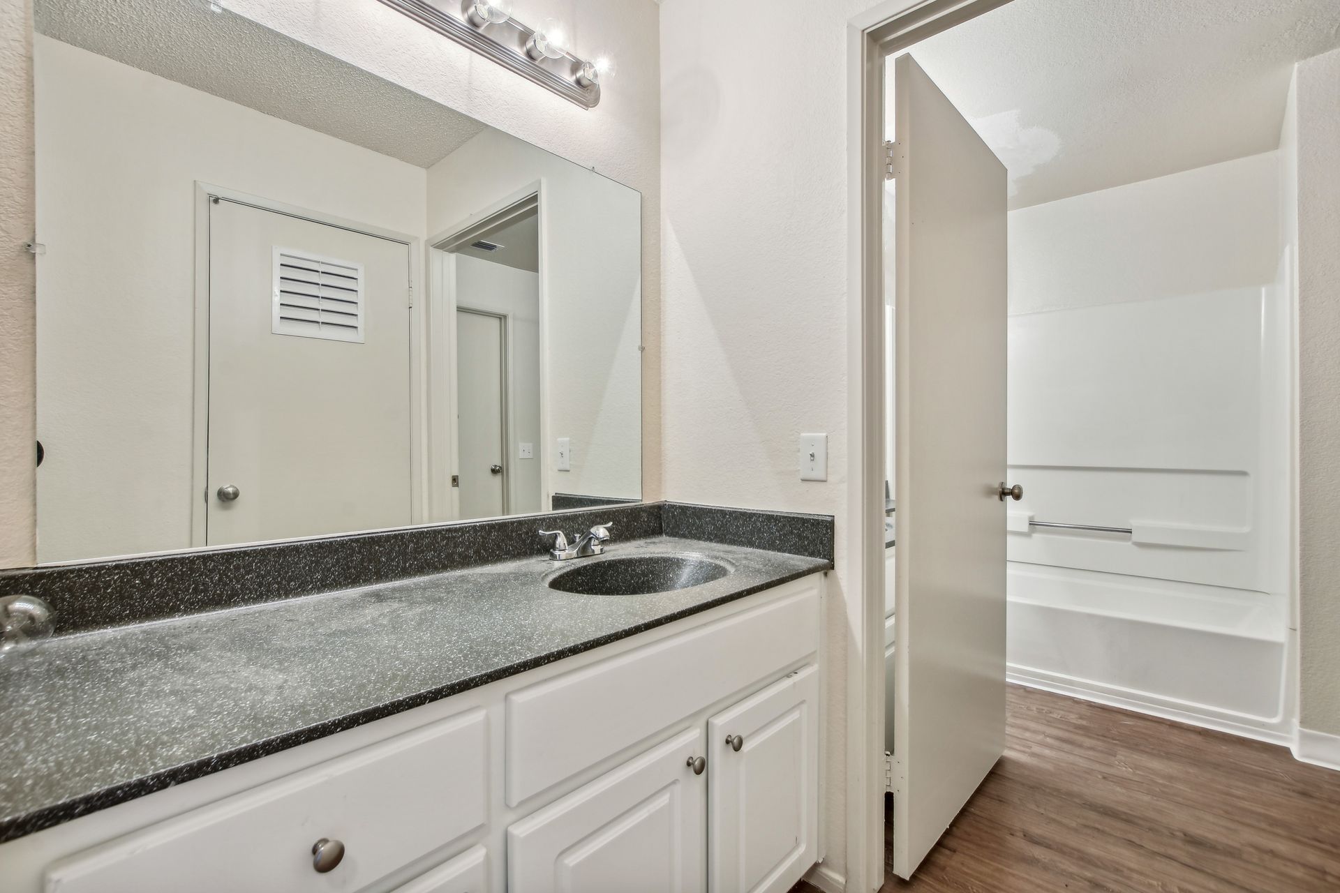 Bathroom with a white vanity, black countertop, and an open doorway to a shower/tub.