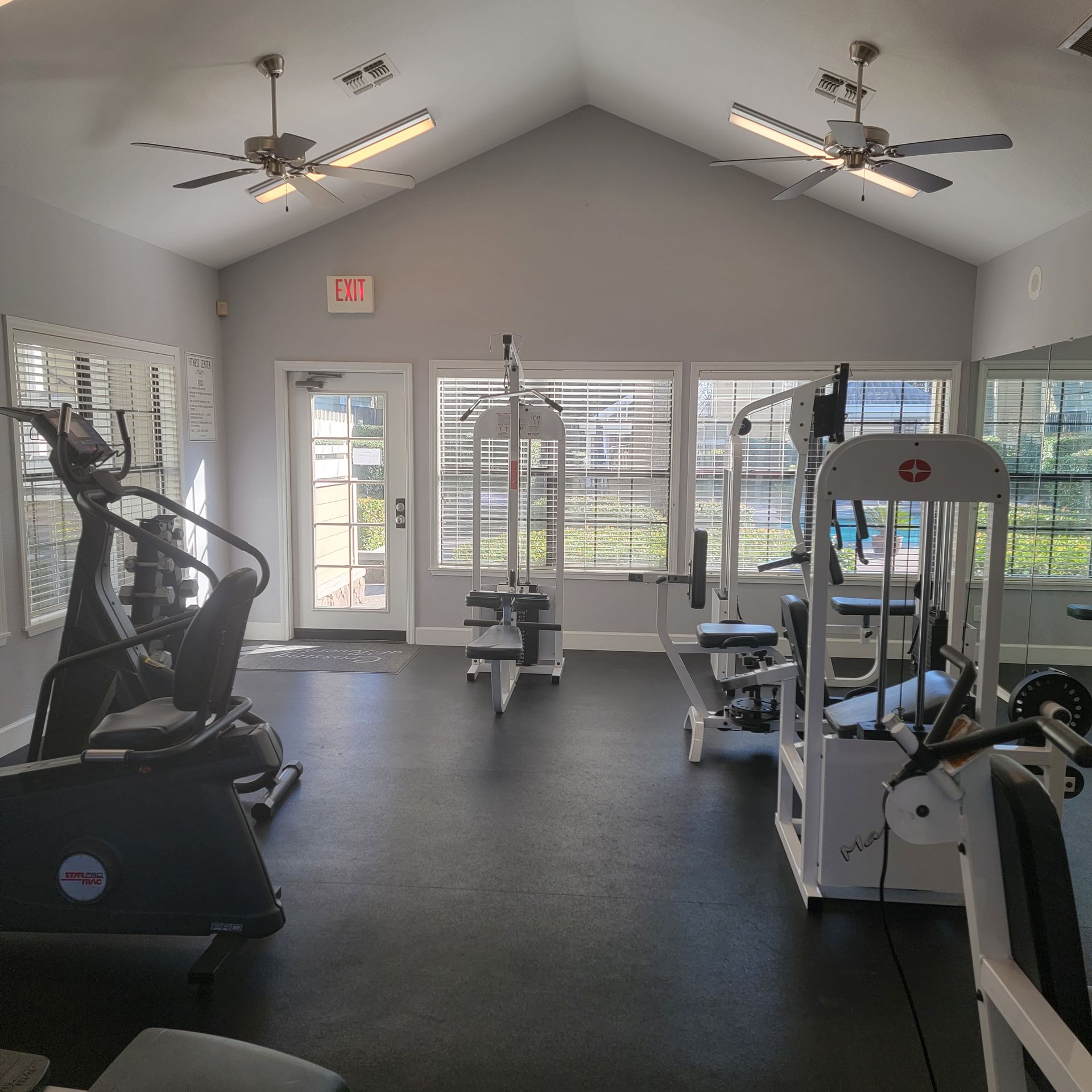 Gym interior with various exercise machines, windows, and ceiling fans.