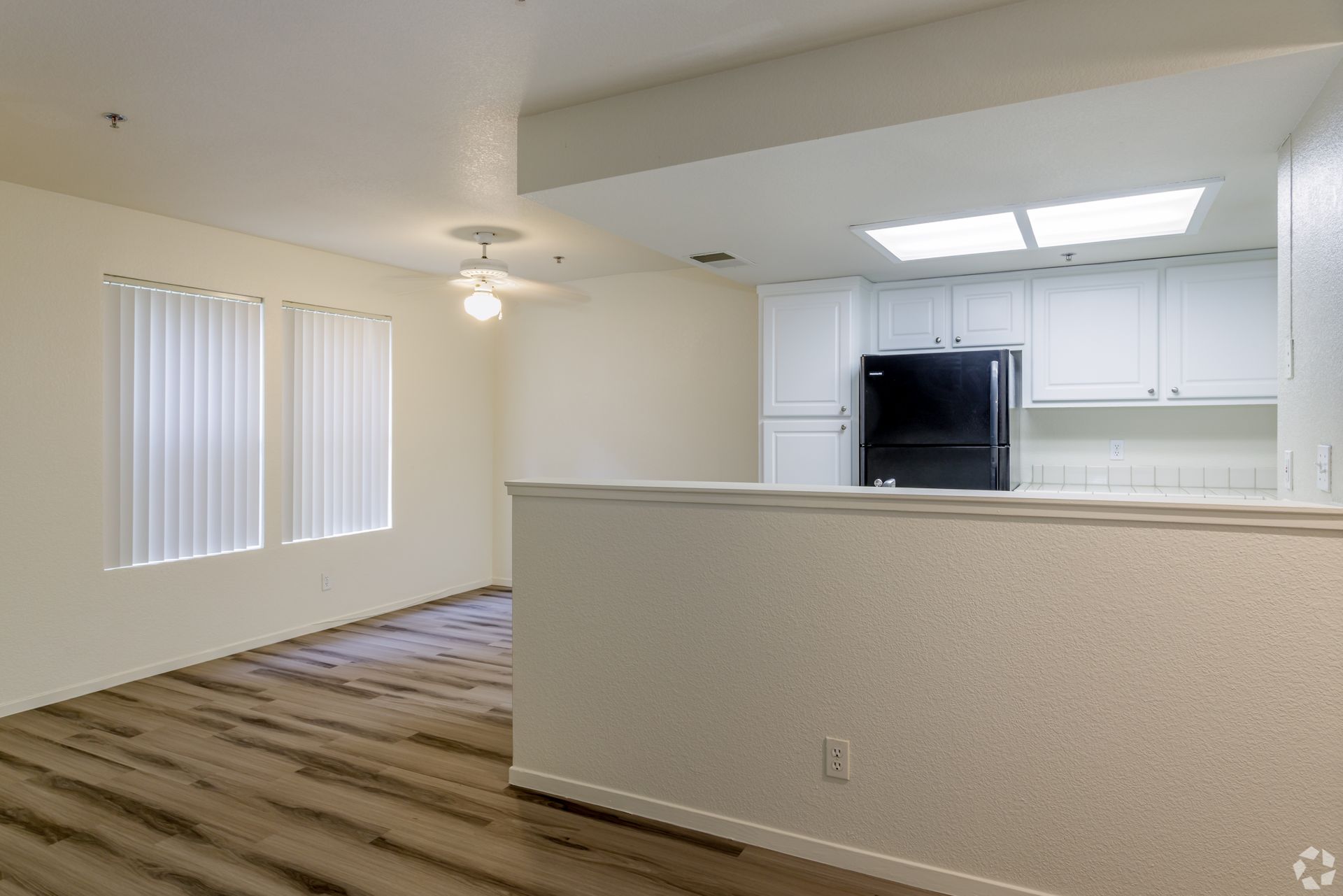 Interior of an apartment with a kitchen, living area, white walls, and wood-look flooring.