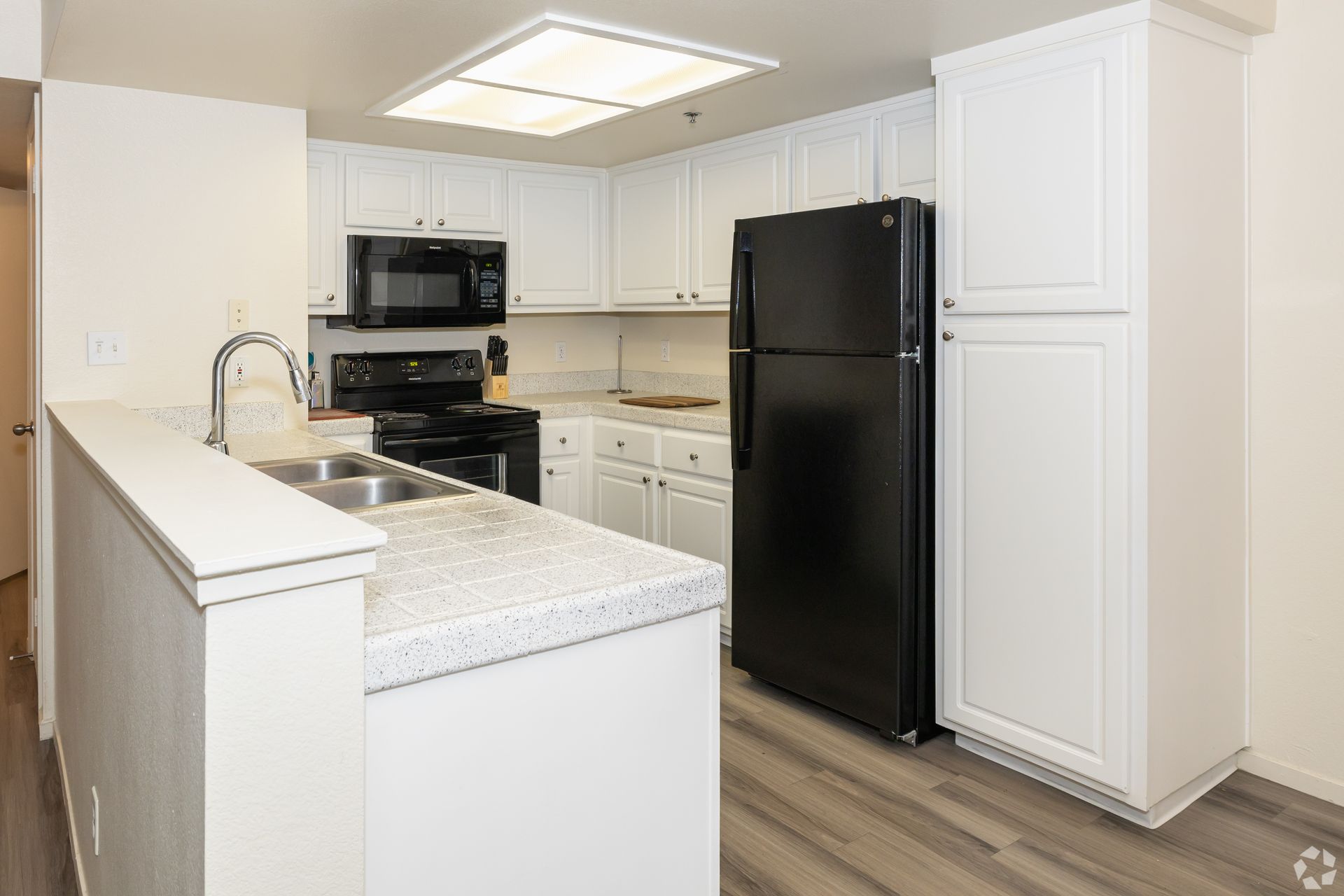 White kitchen with black appliances, including fridge, stove, and microwave, countertops, and cabinetry.