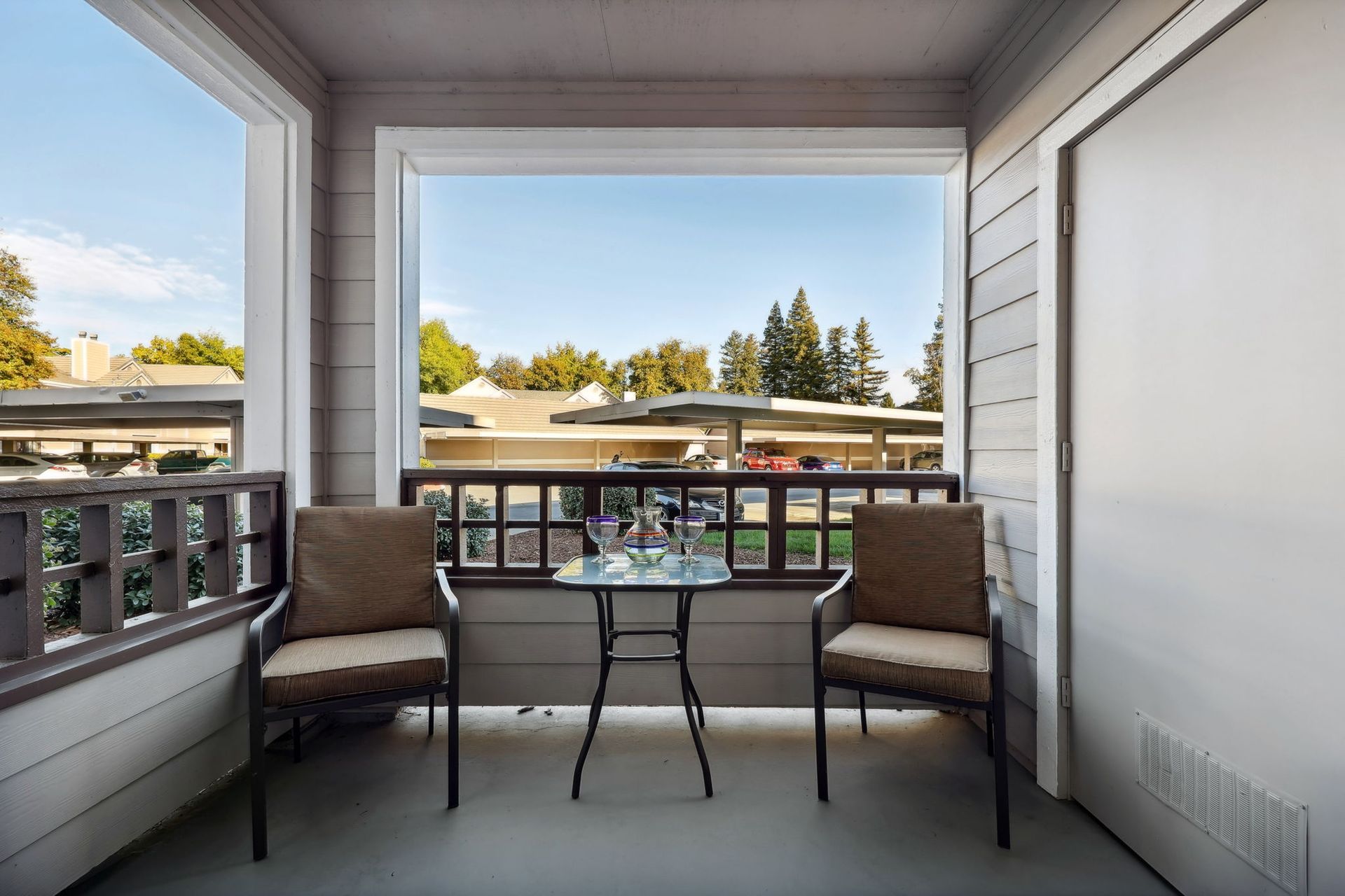 Balcony with two chairs, small table, and a view of buildings and trees.