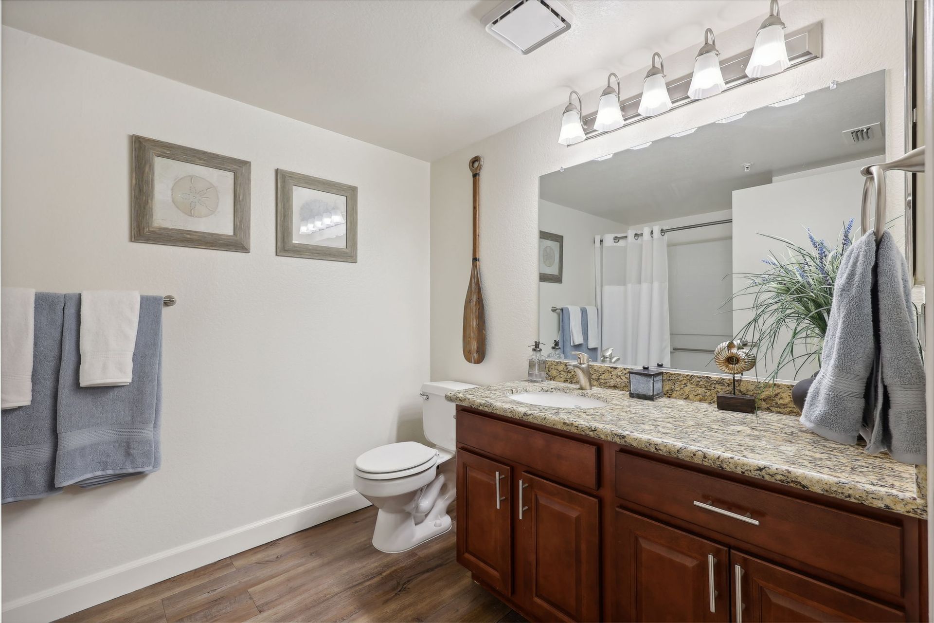 Bathroom with brown cabinets, granite countertop, large mirror, and decorative paddle on the wall.