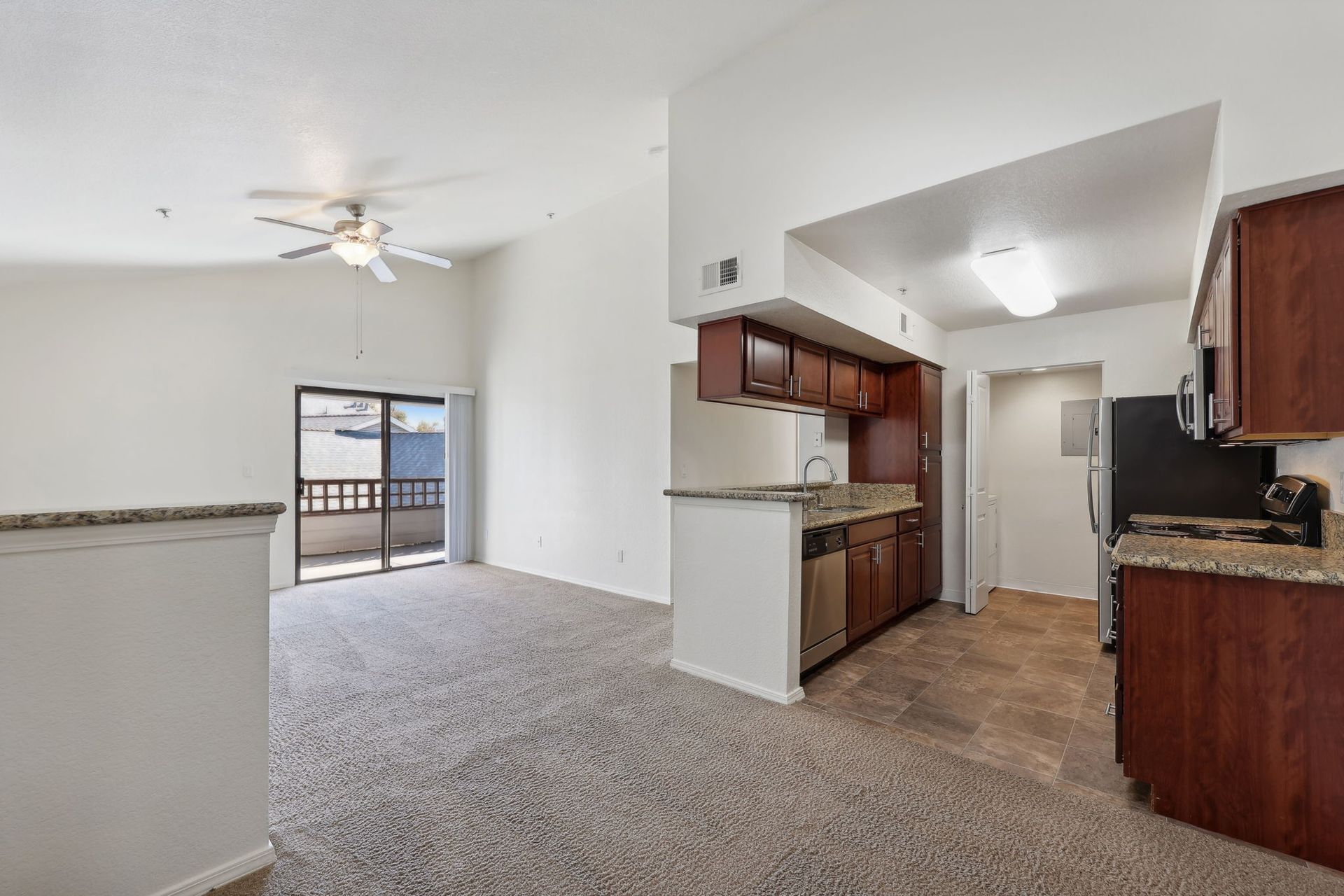 Open-concept apartment with brown cabinetry, granite countertops, and a balcony.