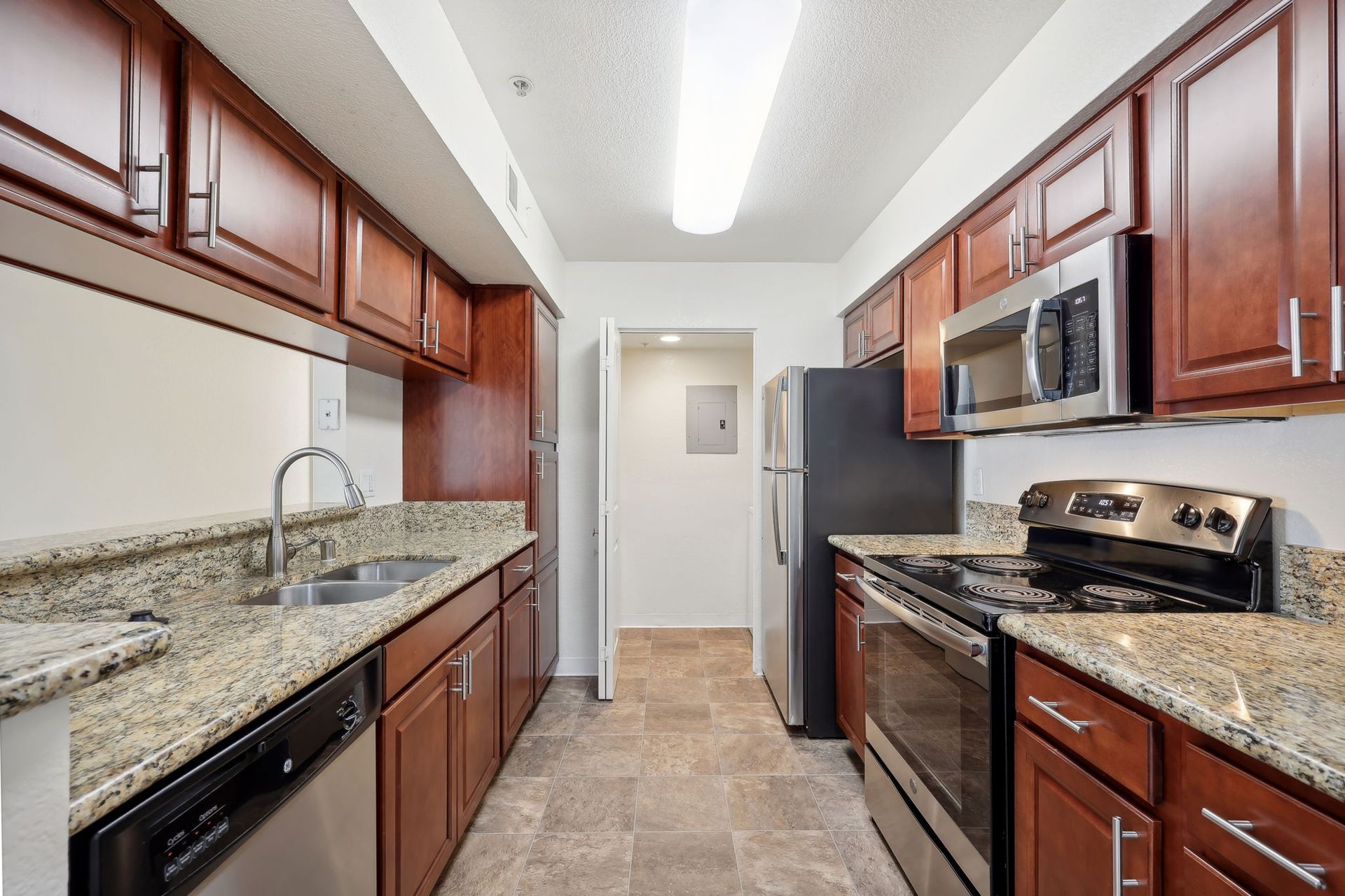 Narrow kitchen with dark wood cabinets, stainless steel appliances, and granite countertops.