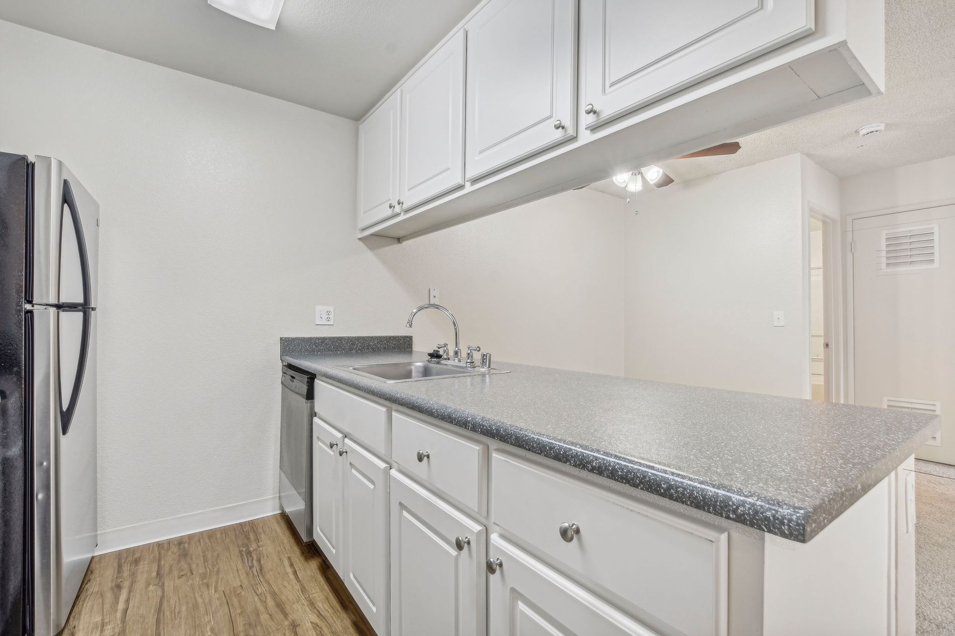 Kitchen with white cabinets, gray countertop, stainless steel appliances, and wood flooring.