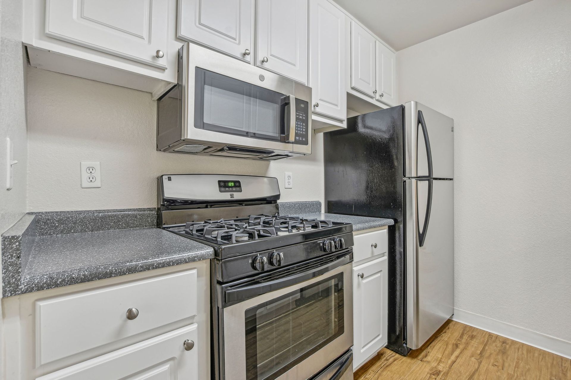 Kitchen with white cabinets, stainless steel appliances, dark countertops, and wood-look flooring.