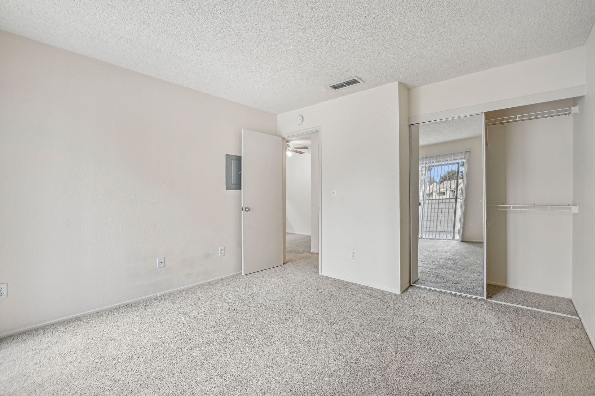 Empty bedroom with carpet, a closet with mirrored doors, and a door leading to a hallway.
