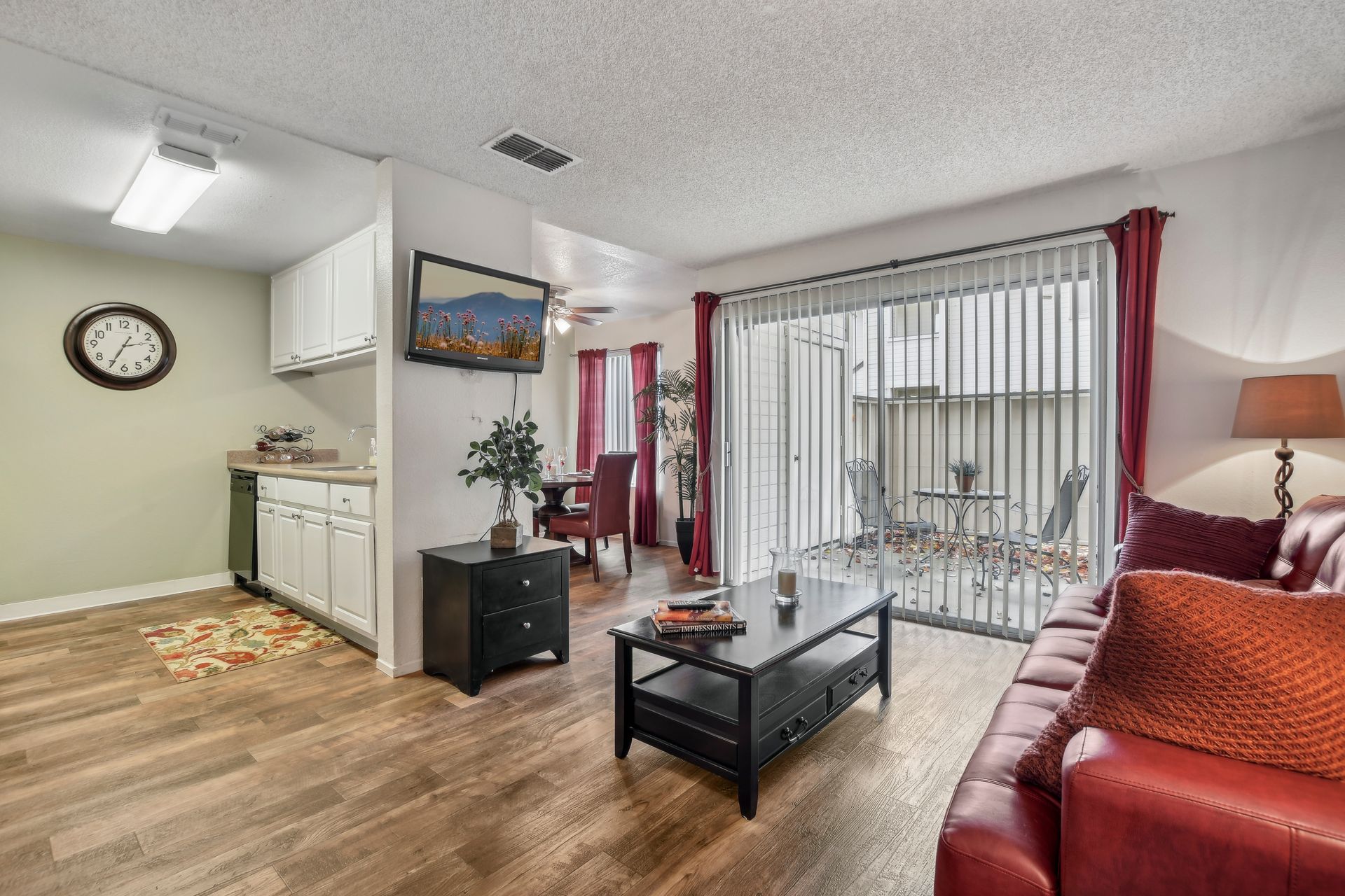 Living room with red couch, table, and sliding door to patio. Clock and TV visible.