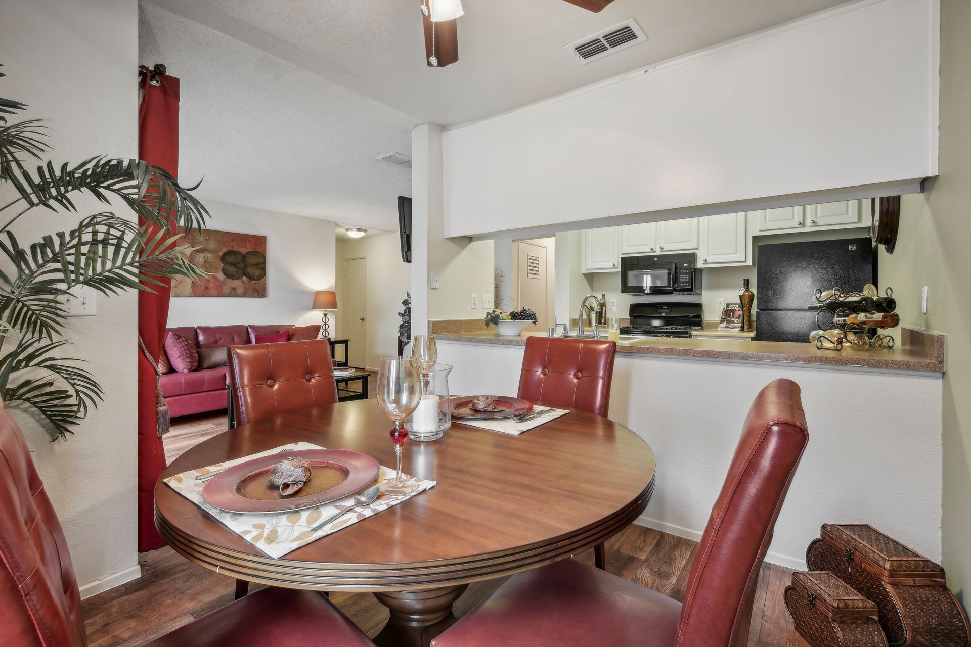 Dining room with round table and red chairs, open to a kitchen, red sofa in the background.