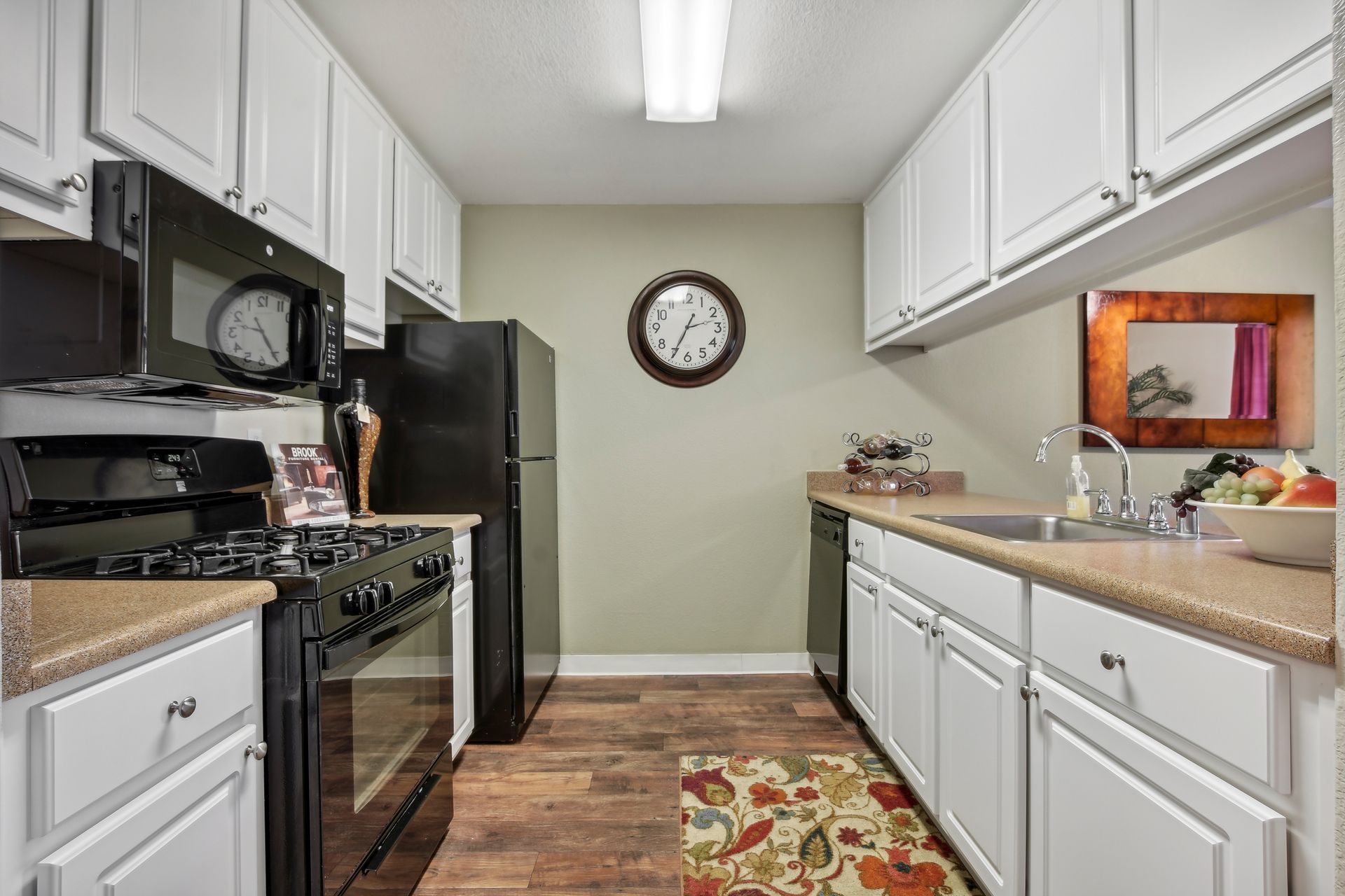 Narrow kitchen with white cabinets, black appliances, and wooden floors.